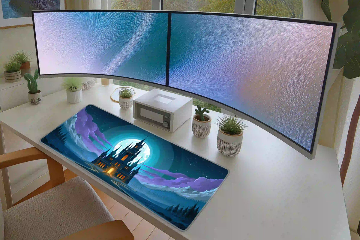 Moonlit gothic castle mat beneath two monitors, with the blue mountain panorama and glowing castle centered on the desk