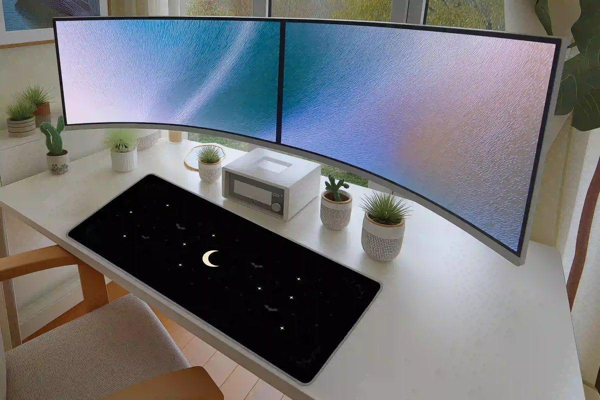 Minimal crescent moon desk mat displayed beneath two monitors, with a pale moon and tiny stars on black