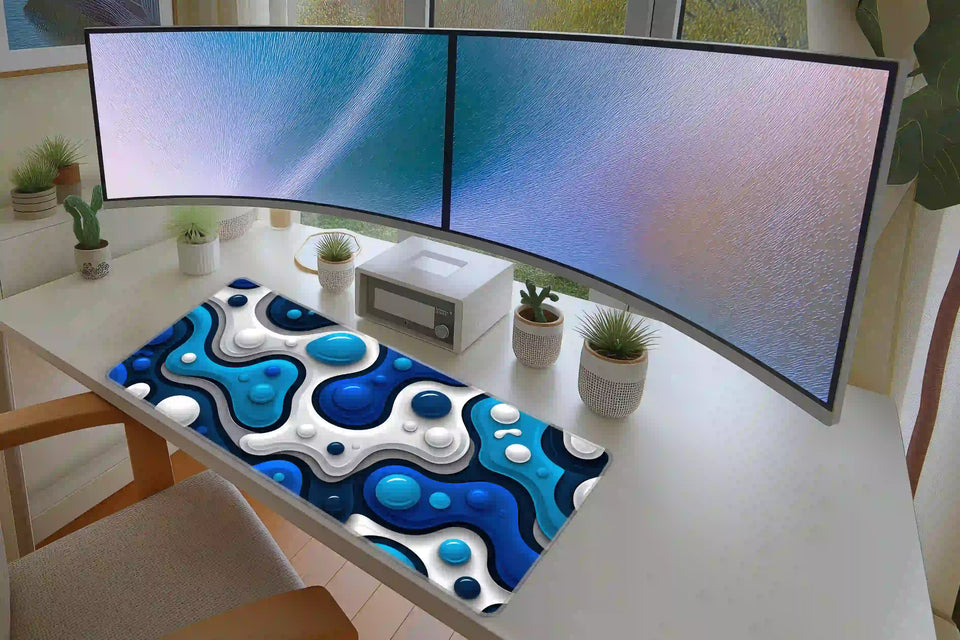 Blue liquid bubble desk mat on a white desk below two monitors, showing blue and white layered abstract artwork