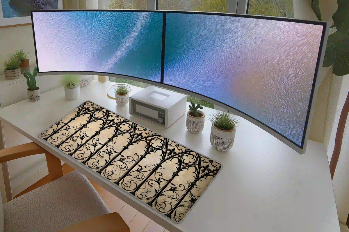 Gothic cathedral arch desk mat displayed beneath two monitors, showing the black ornamental pattern on cream