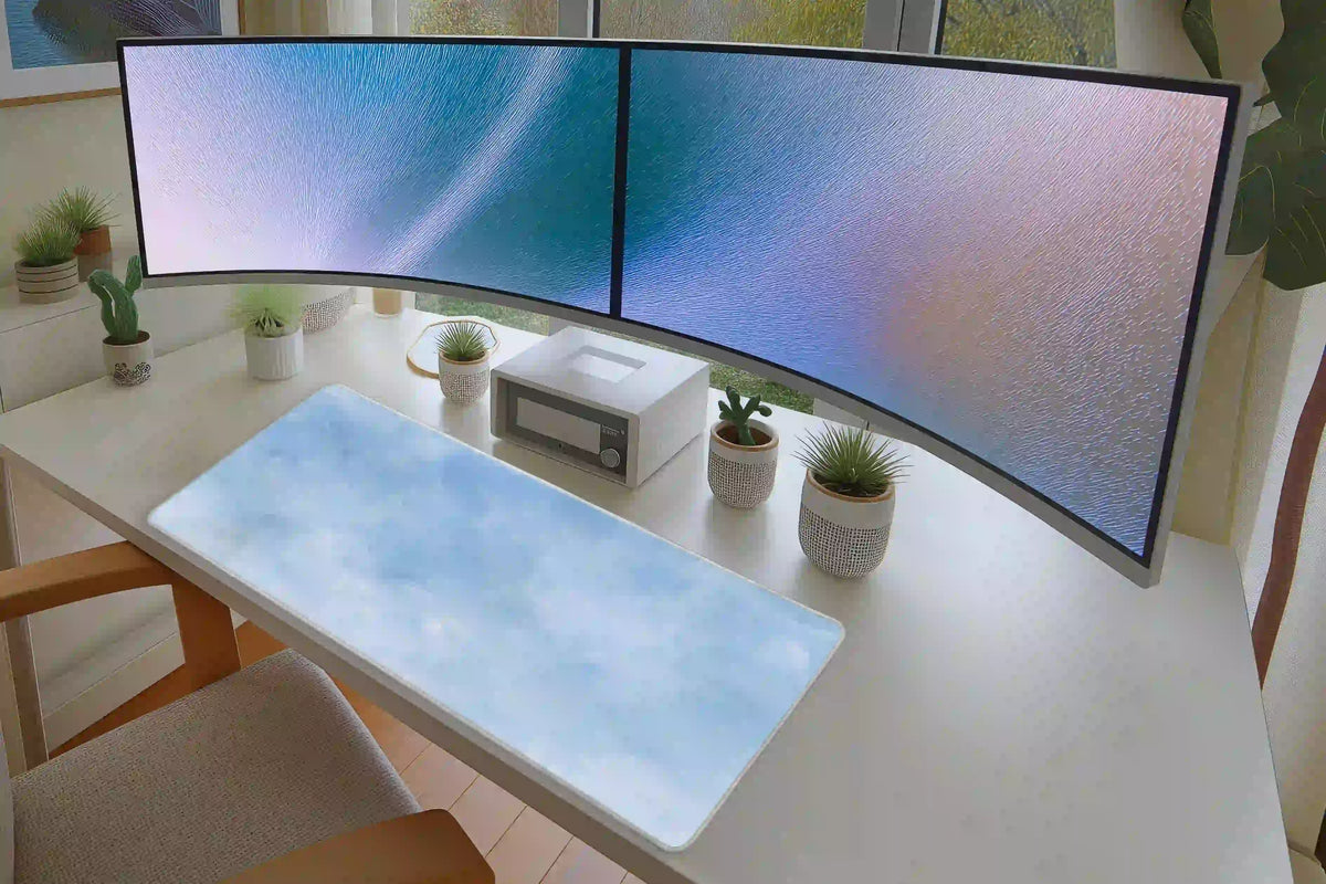 Soft blue watercolor cloud desk mat in a bright white desk setup beneath dual monitors and small plants