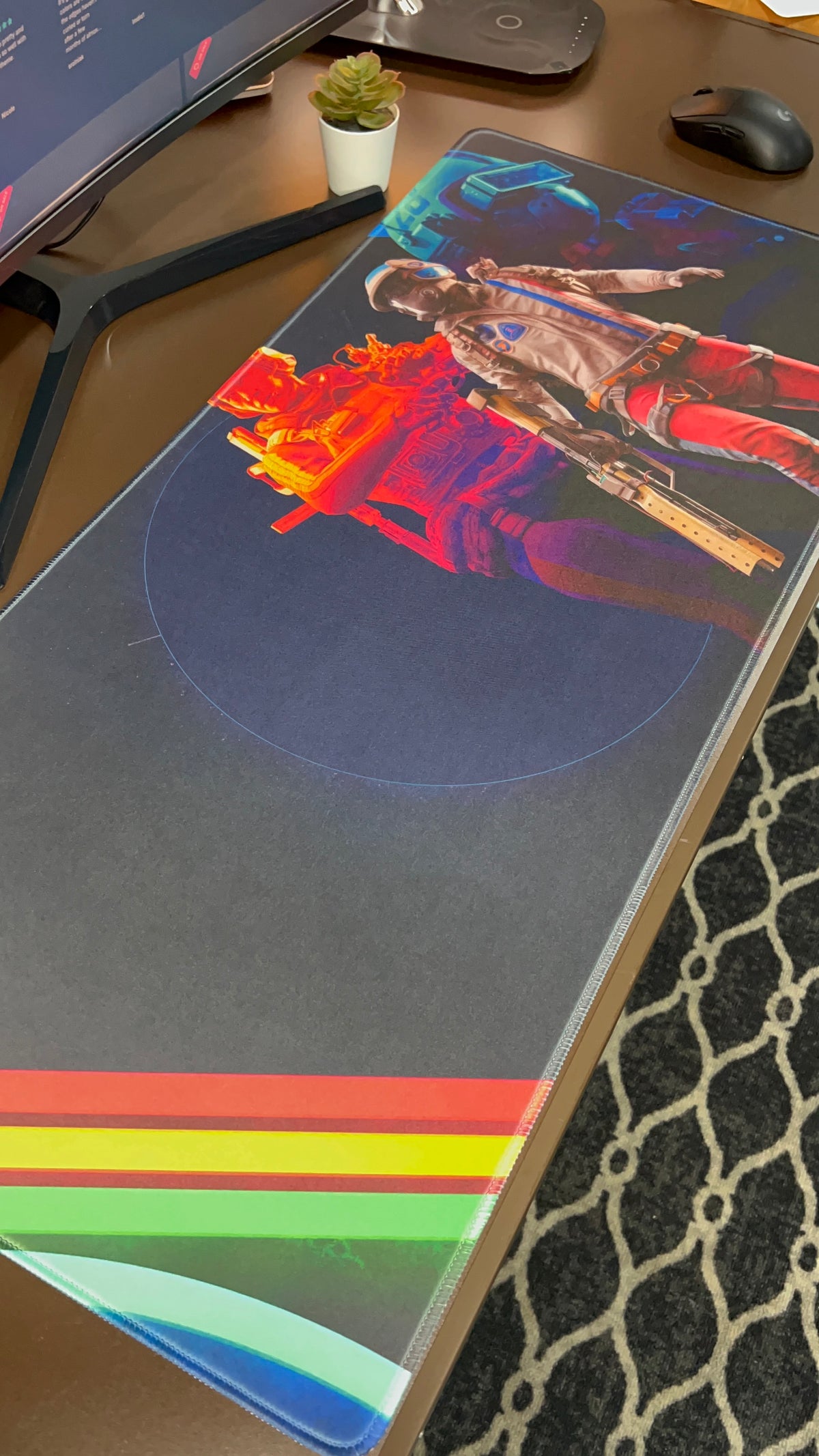 Large custom desk mat on a brown desk, printed with a guitarist, neon red and blue artwork, and rainbow stripes along one end.