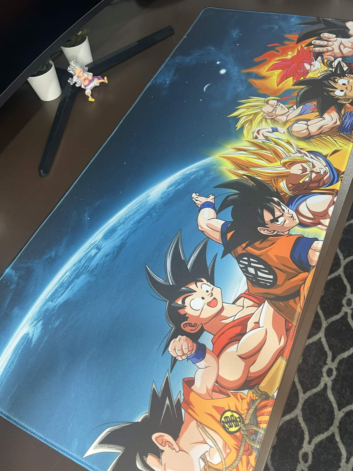 Extended desk mat featuring Goku in multiple Dragon Ball forms against Earth and a starry blue space background.