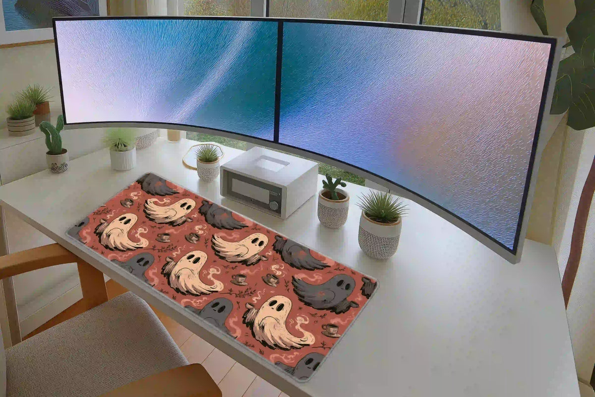 Coral coffee ghost mat on a white desk below monitors, with cream and gray ghosts and scattered cups visible