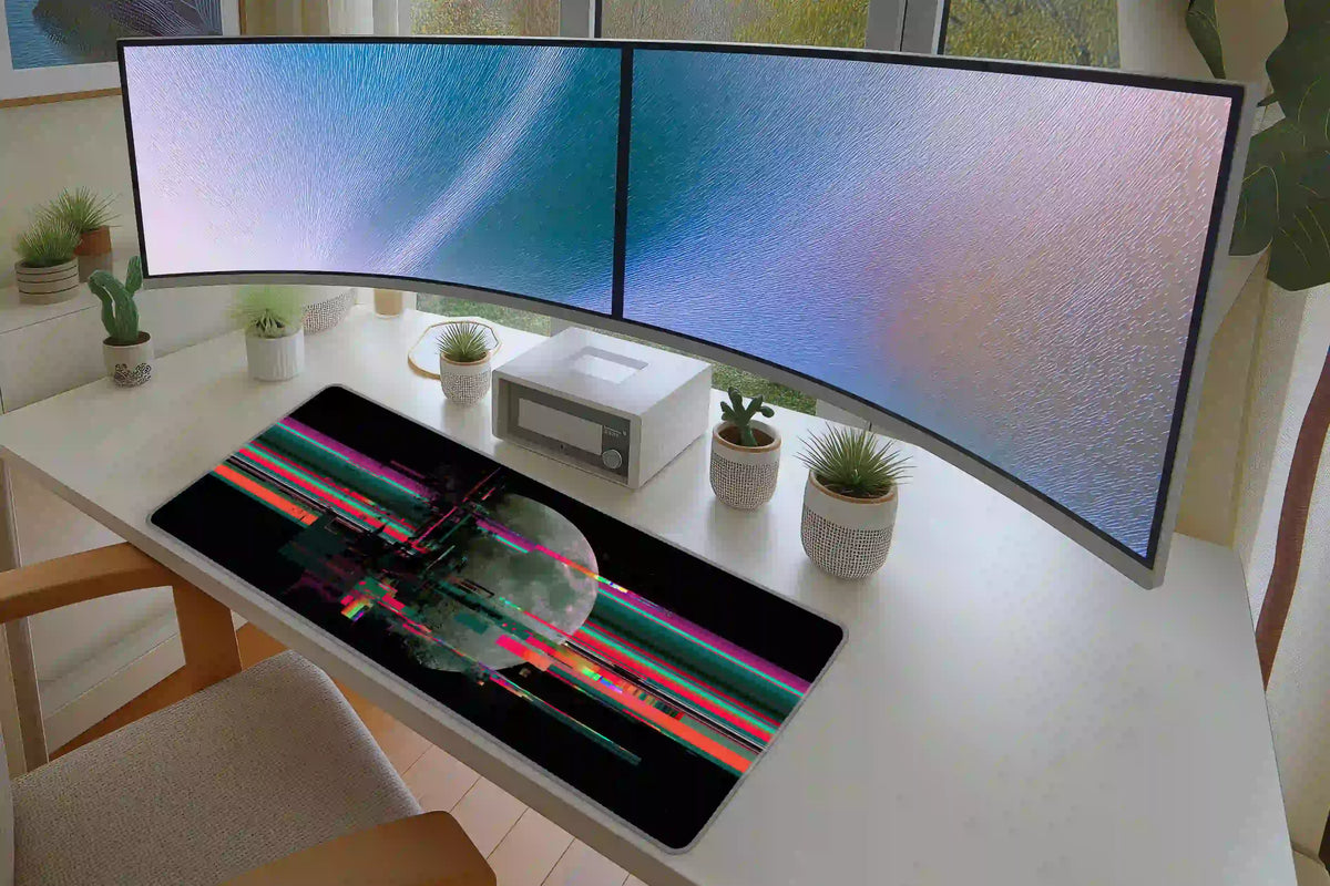 Glitch moon desk mat beneath curved monitors on a white desktop, showing neon digital bands across the lunar artwork