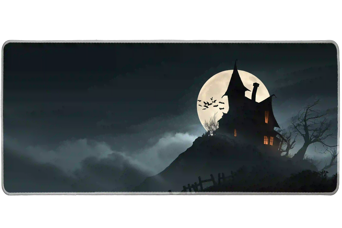 Haunted house desk mat with a black crooked mansion, orange windows, bats, gray fog and a pale full moon