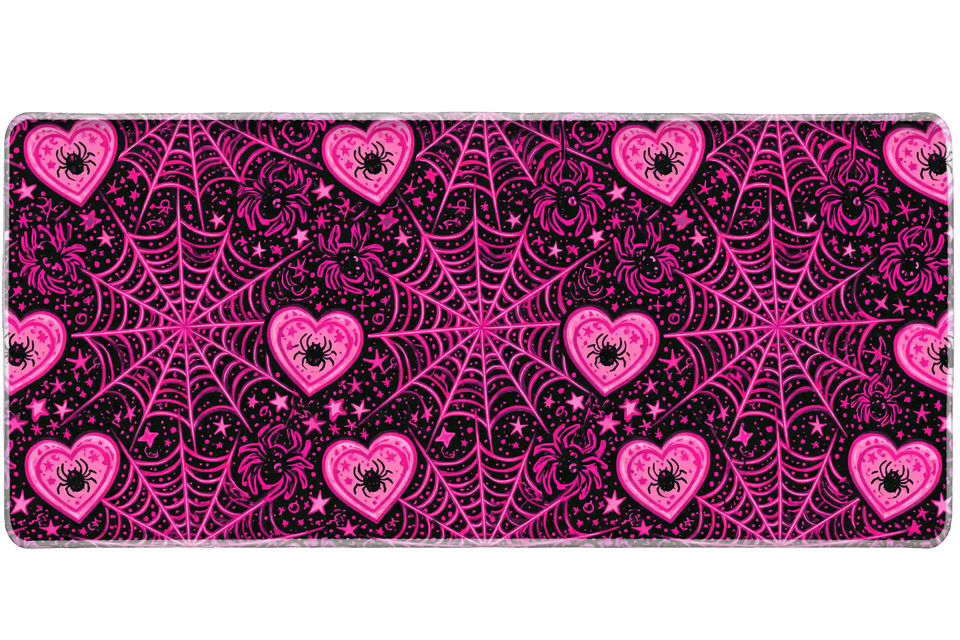 Black and hot pink desk mat patterned with spiderwebs, spiders inside hearts and scattered stars